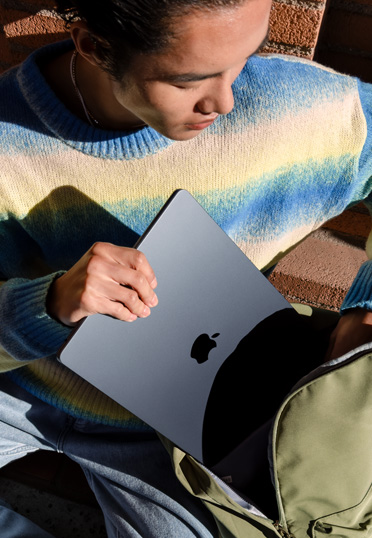一名學(xué)生坐在外面。他從書包里拿出一臺封閉的 MacBook。